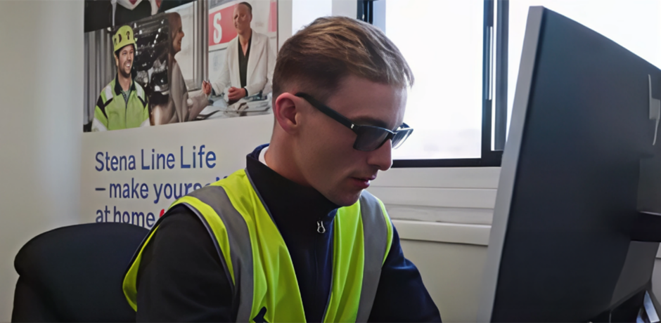 A man wearing a high-viz vest sits at a computer.