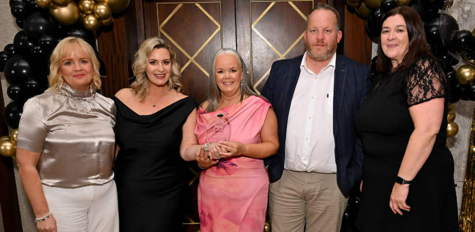 Five people standing together. One is holding an award.
