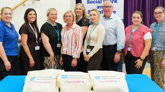 A group of people standing behind a table. On the table there are bags with Team North branding.