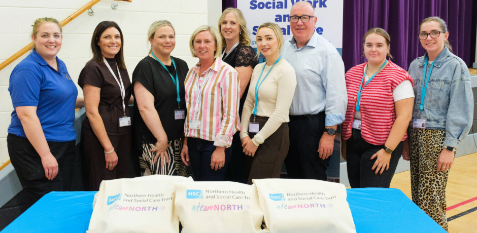 A group of people standing behind a table. On the table there are bags with Team North branding.