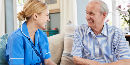 A nurse wearing a blue tunic talks to an older man.