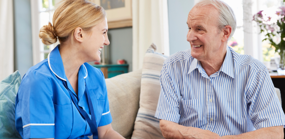A nurse wearing a blue tunic talks to an older man.