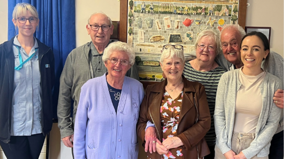 Two staff members standing with five older people