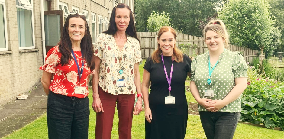 Four women standing together in a garden area.