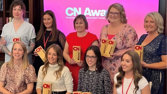 A group of people, some are sitting and some are standing behind. Each person is holding a trophy branded with CN Nutrition.