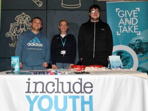 Three people standing behind a table with include youth written on it.