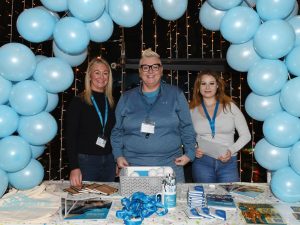 Three people standing under balloon arch with promotional items on the table in front of them