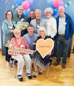 A large group of people sitting and standing together with signs reading "Volunteers' Week" and "Thank You".
