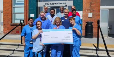 A group of hospital staff wearing blue scrubs standing together, holding a large cheque.