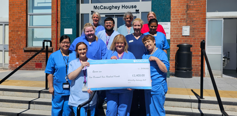 A group of hospital staff wearing blue scrubs standing together, holding a large cheque.