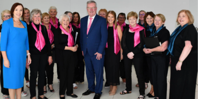 Members of the Rural Melody Ladies Choir, dressed in black with pink scarves, with Northern Trust Chief Executive Jennifer Welsh and Health Minister Mike Nesbitt.
