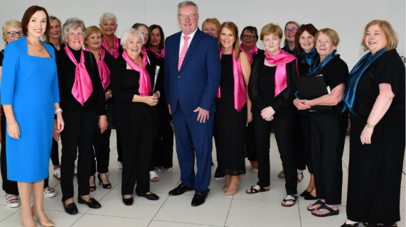 Members of the Rural Melody Ladies Choir, dressed in black with pink scarves, with Northern Trust Chief Executive Jennifer Welsh and Health Minister Mike Nesbitt.