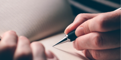 Person holding a pen and writing in a book.