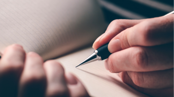 Person holding a pen and writing in a book.