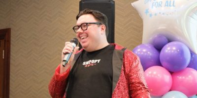 A man sings while wearing a red sparkly jacket.