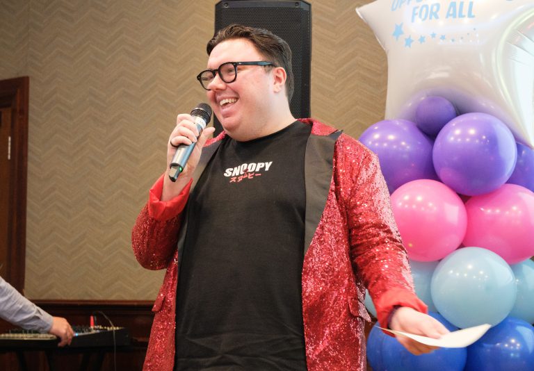 A man sings while wearing a red sparkly jacket.