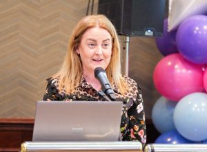 A woman speaks into a microphone, with a laptop in front of her.