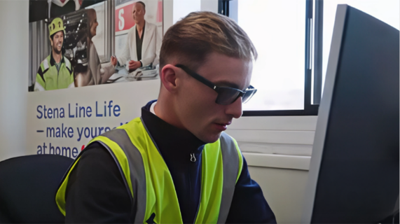 A man wearing a high-viz vest sits at a computer.