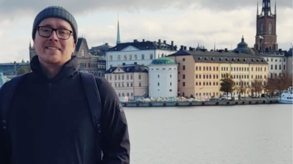 Dean Polly, with a river and buildings behind him.