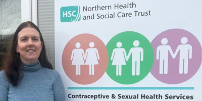 Dr Sharon Porter standing outside a building, beside a sign for Contraceptive and Sexual Health Services.