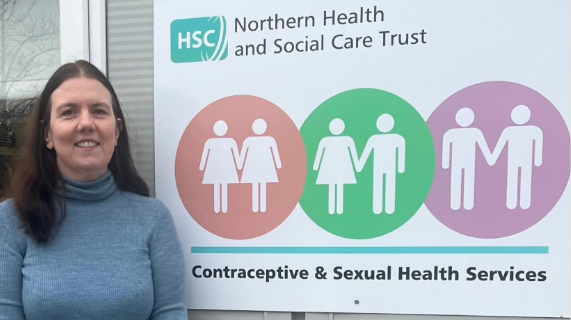 Dr Sharon Porter standing outside a building, beside a sign for Contraceptive and Sexual Health Services.