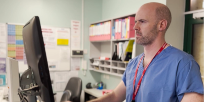A consultant wearing blue scrubs looks at a computer screen.