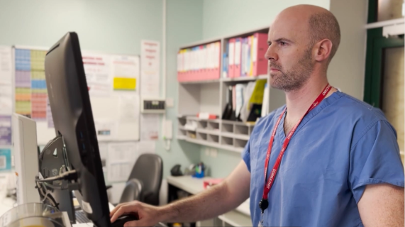 A consultant wearing blue scrubs looks at a computer screen.