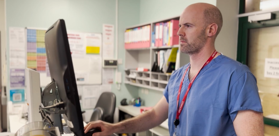 A consultant wearing blue scrubs looks at a computer screen.