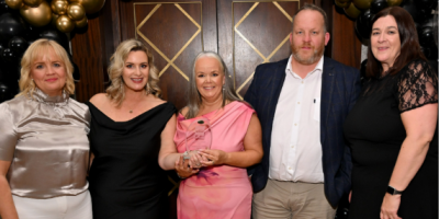 Five people standing together. One is holding an award.