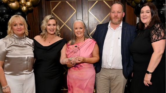 Five people standing together. One is holding an award.