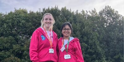 Hazelle Ongcoy and Caillee McHugh standing together outside. They are wearing matching pink jumpers and there are trees behind them.