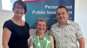 Two women and a man standing in front of a pop-up banner.