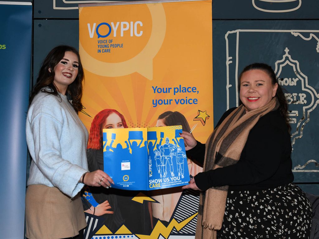Two women standing in front of a display stand holding a document