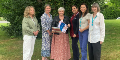 Six women standing together outside. One lady is holding a booklet.