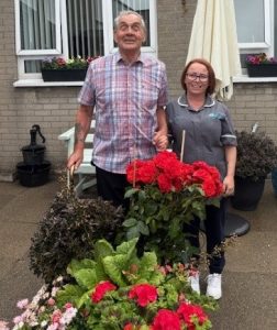 Photograph of Inniscoole Service User and member of staff standing in front of the plants and flowers on display in Inniscoole.
