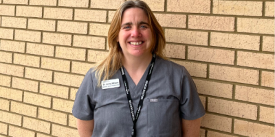 Dr Jennifer Wilson wearing a grey uniform standing against a brick wall.