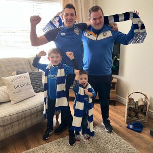 Two adults and two children with blue and white football scarves and wearing blue tops.