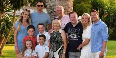 Seven adults and 4 children standing in front of a palm tree.