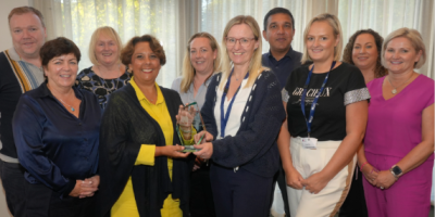 Ten people standing together. One lady in the group is receiving an award from another lady.