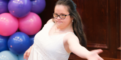 A young girl with Down Syndrome dances, with a display of balloons in the background