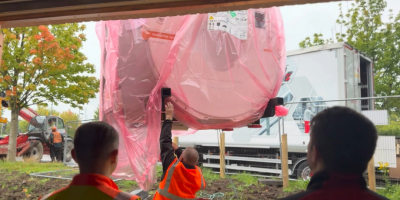 An MRI scanner wrapped in red plastic is lowered to the ground while workers look on.