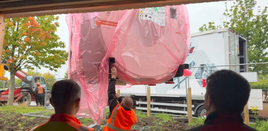 An MRI scanner wrapped in red plastic is lowered to the ground while workers look on.