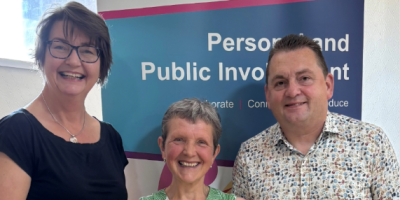 Two women and a man standing in front of a pop-up banner.