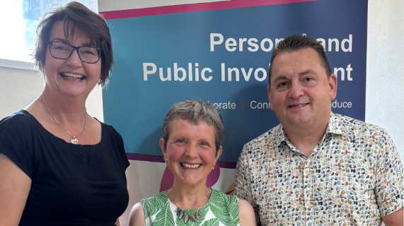 Two women and a man standing in front of a pop-up banner.