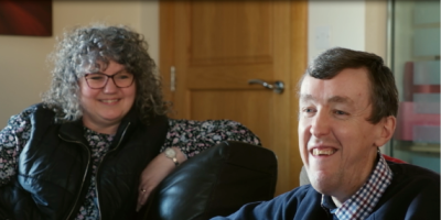 A man and woman sitting together, both are smiling.