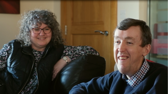 A man and woman sitting together, both are smiling.