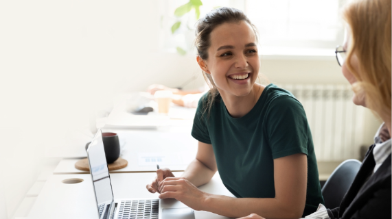 Two women sit together with a laptop in front of them