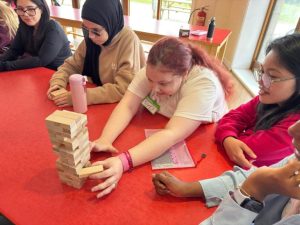Young people sit at a table playing jenga together.