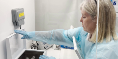 Marie Harvey, Lead Radiographer for Nuclear Medicine, wearing PPI, with a box in front of her with vials inside.