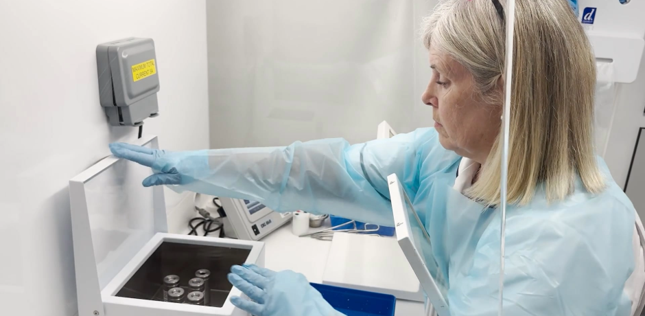 Marie Harvey, Lead Radiographer for Nuclear Medicine, wearing PPI, with a box in front of her with vials inside.